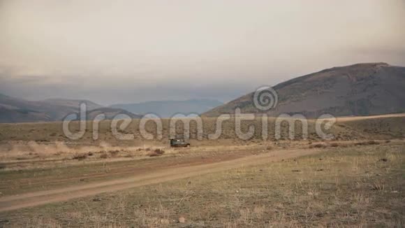 越野车快速驾驶穿越一个平坦的尘埃场白天的背景是山丘和山脉视频的预览图