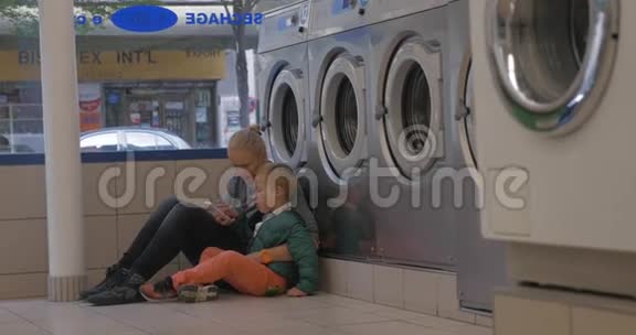 母亲和孩子在洗衣店里使用手机视频的预览图