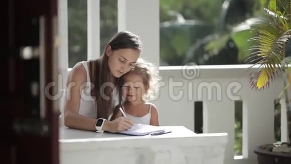 年轻的母亲和女儿在阳台画画背景是棕榈树视频的预览图