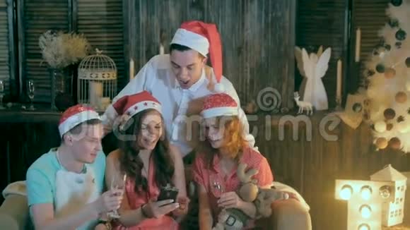 无忧无虑的青少年朋友庆祝圣诞节附近装饰圣诞节观看视频智能手机视频的预览图