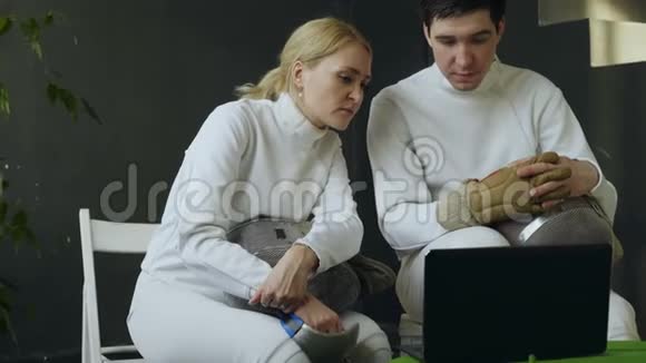 两位年轻的击剑师男女在笔记本电脑上观看击剑教程并在训练前分享经验视频的预览图