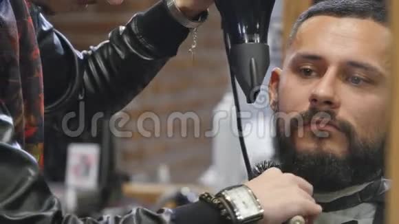 新发型在坐在椅子上的时候年轻的胡须男用吹风机在理发店洗头发视频的预览图