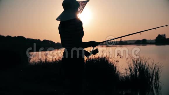 一位年轻女子的剪影她手里拿着一根钓竿在黎明时旋转视频的预览图