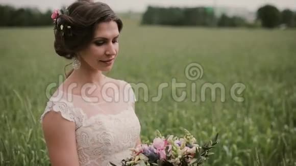 美丽的新娘站在麦田里穿着漂亮的白色连衣裙看着手中的一束花婚礼日视频的预览图