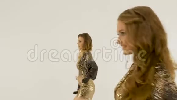 两个漂亮的女孩穿着闪亮的连衣裙在工作室里在白色的背景下跳舞和唱歌视频的预览图