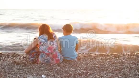 妈妈和两个男孩坐在海滩上儿子在日落时出海视频的预览图