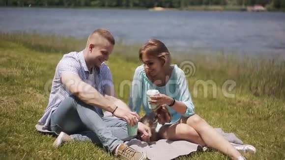 一个男人和一个女孩在河边约会时笑着喝咖啡一只小狗坐在女房东旁边视频的预览图