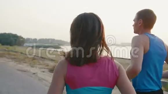 几个年轻的成年运动员日落时一个个女人和一个男人沿着河边跑健康生活方式视频的预览图