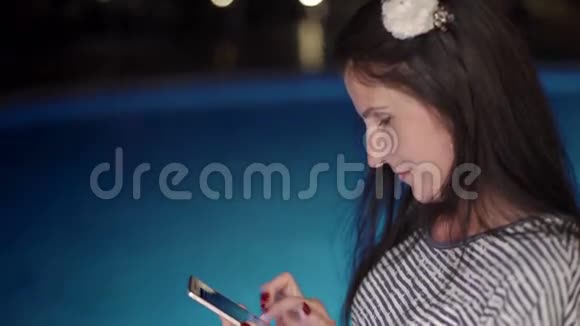 快乐女孩使用智能手机晚上在游泳池附近打字视频的预览图