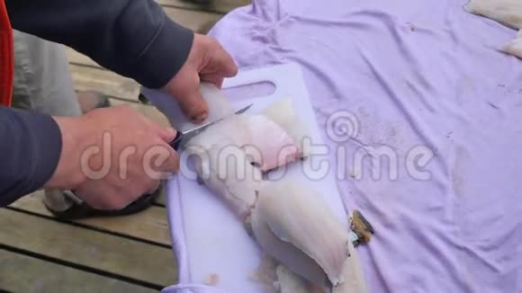 街头海鲜市场烧烤用鱼片切割男手正在准备鱼片把它切成塑料砧板视频的预览图