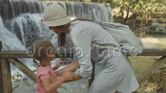一位年轻的母亲和她可爱的女儿靠着瀑布休息视频的预览图