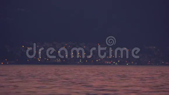 傍晚美丽的海景遥远的城市灯光平静的水迷人的风景一艘小船航行视频的预览图