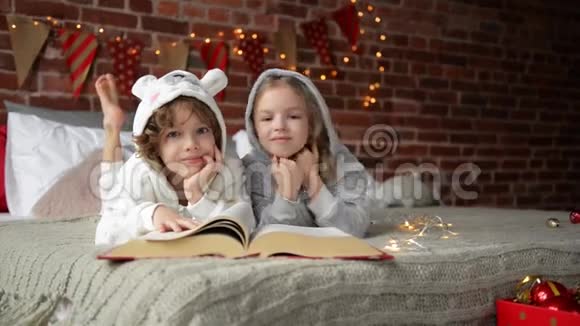 快乐可爱的孩子们穿着温暖的圣诞睡衣笑着看着相机微笑的孩子们在看书视频的预览图