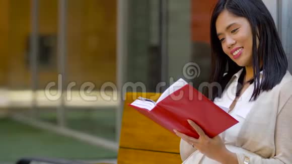 微笑的亚洲女人坐在长凳上看书视频的预览图