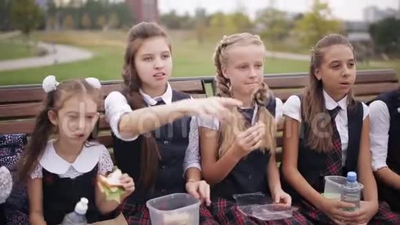 女大学生穿着相同的校服在公园休息时吃三明治微笑视频的预览图