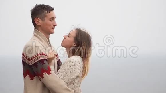 一对年轻迷人的夫妇穿着针织毛衣在海边的悬崖上取笑拥抱和亲吻视频的预览图