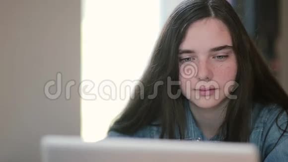 使用笔记本电脑坐在家里餐桌上的少女特写肖像视频的预览图