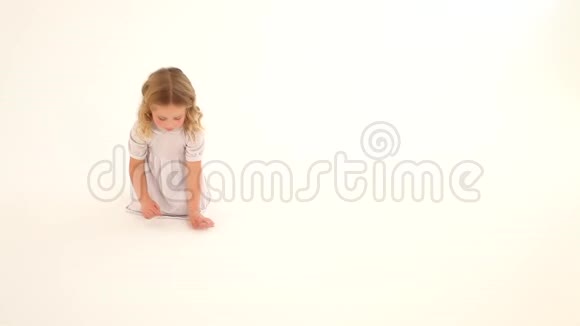 婴儿小孩学步女孩玫瑰色脸颊金发卷发白色连衣裙坐着画心手指地板白色背景视频的预览图