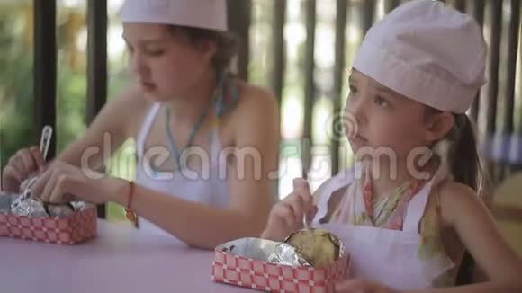 两个小女孩以厨师的形式坐在桌子旁吃他们煮的热土豆视频的预览图