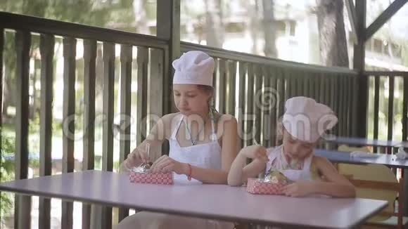 两个小女孩以厨师的形式坐在桌子旁吃他们煮的热土豆视频的预览图