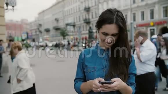 现代技术美丽的黑发年轻女子穿着牛仔裙在繁忙的街道上使用她的智能手机慢节奏视频的预览图