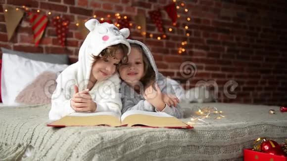 快乐可爱的孩子们穿着温暖的圣诞睡衣笑着看着相机微笑的孩子们在看书视频的预览图