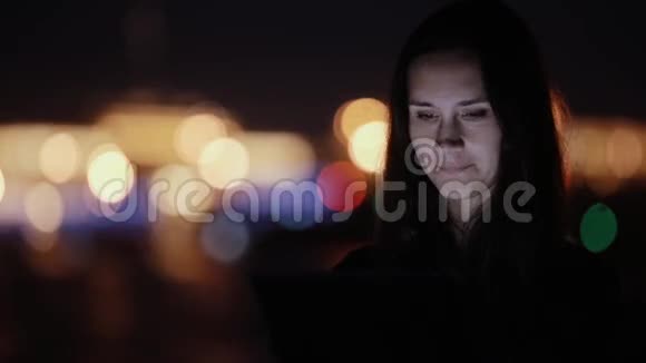 夜城漂亮的年轻女人用平板电脑微笑背景上模糊的彩色城市灯光现代技术视频的预览图