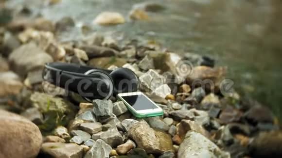 耳机和智能手机躺在海边的岩石上拍打着海浪视频的预览图