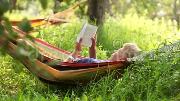 男人在树影下舒适的吊床上看书视频的预览图