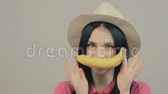 嘲笑健身女人拿着香蕉在灰色背景上露出拇指看着摄像机视频的预览图