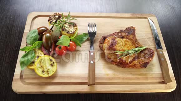 骨头上的烤猪肉牛排和厨房用具的木板上的蔬菜视频的预览图