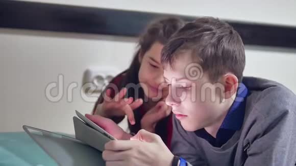 男孩和室内一个女孩在玩平板电脑兄妹儿童社交媒体在线游戏平板电脑视频的预览图