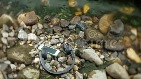 耳机和智能手机躺在海边的岩石上拍打着海浪视频的预览图