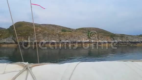 游艇在平静的水域沿着石岸航行绑在缆绳上的红丝带随风飘散视频的预览图