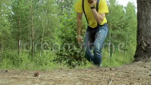 徒步旅行者穿过森林打电话黄色T恤和带有吊带的牛仔裤技术视频的预览图