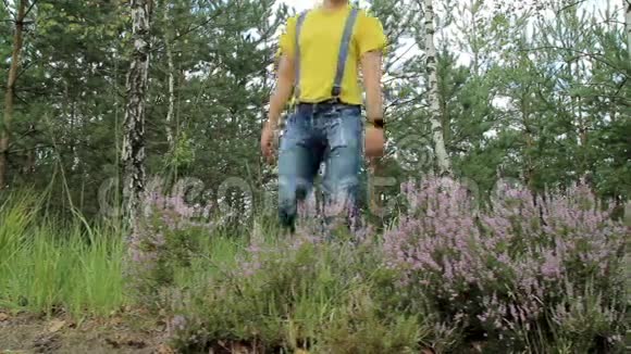 徒步旅行者穿过森林触摸智能手表黄色T恤和带有吊带的牛仔裤技术视频的预览图