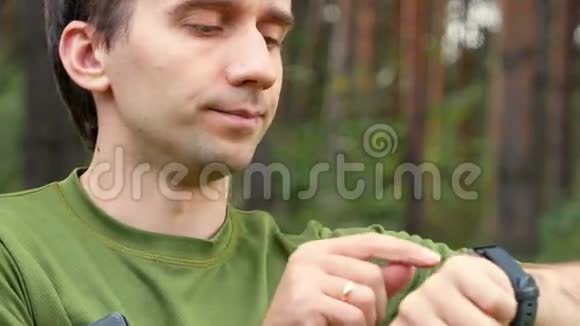 年轻人在公园里触摸可穿戴设备绿色T恤阅读留言面带微笑特写视频的预览图