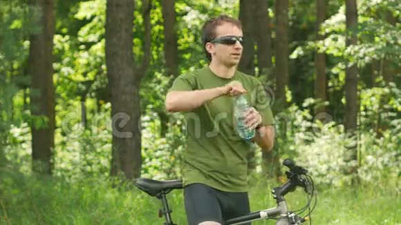 年轻的骑自行车的男性从公园里的瓶子里喝水绿色T恤和太阳镜视频的预览图