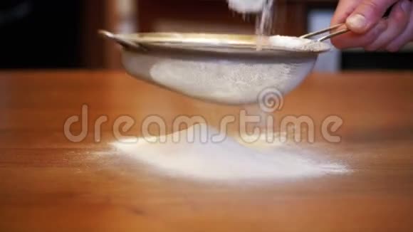 在家庭厨房的木桌上通过筛子筛面粉慢动作视频的预览图