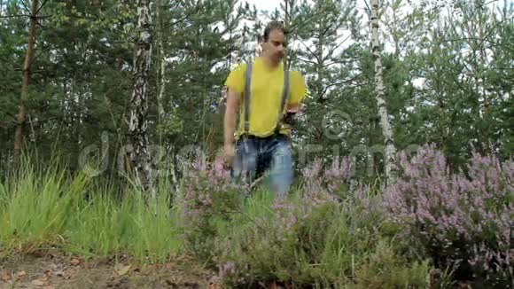 徒步旅行者穿过森林打电话黄色T恤和带有吊带的牛仔裤技术视频的预览图