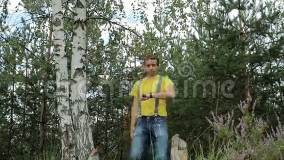 徒步旅行者穿过森林触摸智能手表黄色T恤和带有吊带的牛仔裤技术视频的预览图