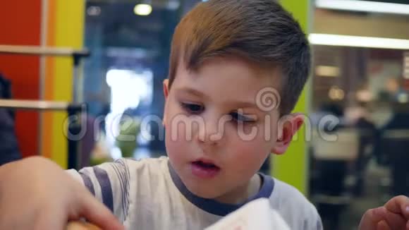 小男孩在儿童餐厅吃饭时胃口大开儿童晚餐吃食物午餐吃薯条和汉堡视频的预览图