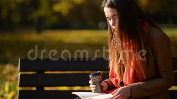 美丽的高加索女人在秋季公园的长凳上喝咖啡和看书户外放松的概念视频的预览图