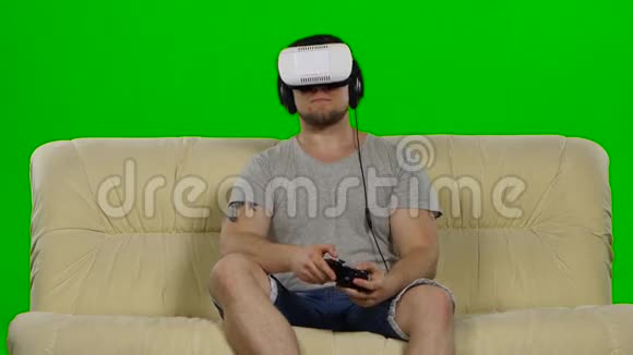 沙发上的年轻帅哥戴着VR耳机眼镜绿色屏幕视频的预览图