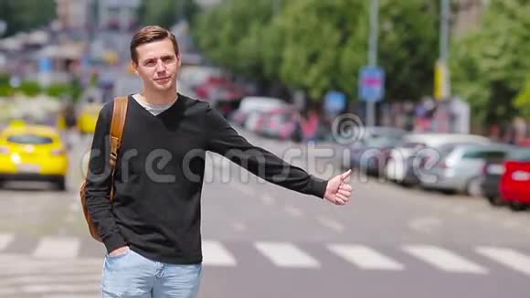 年轻的快乐男子在欧洲的街道上搭出租车一位带背包的白种人游客微笑着抓着一个视频的预览图