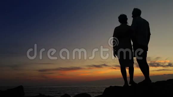 在岩石海岸线上亲吻一对夫妇伴着日落日出视频的预览图