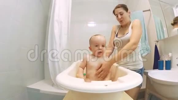 美丽慈爱的母亲亲吻她的小儿子在塑料浴缸里洗澡视频的预览图