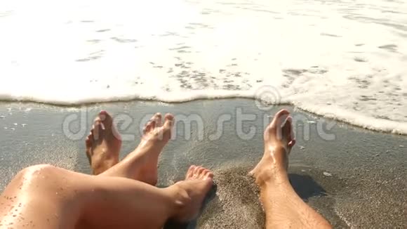 一对夫妇坐在海滩上合上双脚和波浪慢动作4k视频的预览图