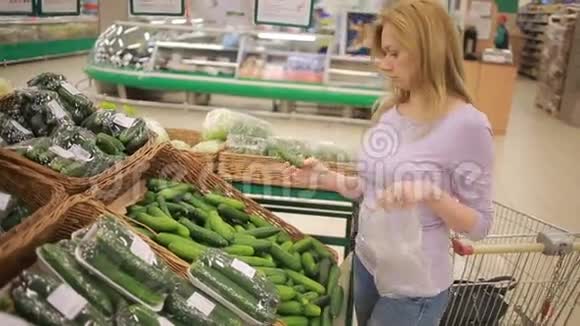一个女人在超市的蔬菜货架上买蔬菜黄瓜视频的预览图