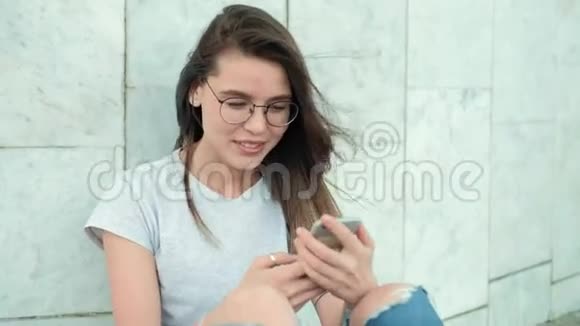 一位戴着黑色背包眼镜的黑发女孩坐在灰色大理石墙上挺直头发笑起来很高兴视频的预览图